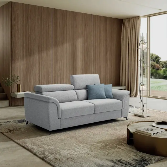 Divano letto Aquila grigio chiaro in un soggiorno con parete in legno e grande vetrata