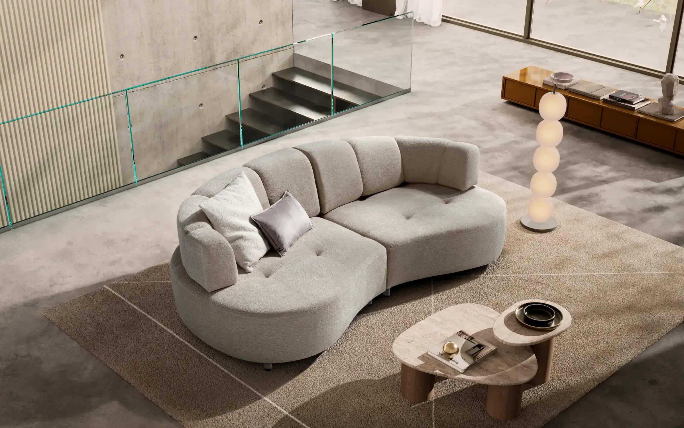 Divano Curved in un living luminoso con scala in vetro, visto dall’alto