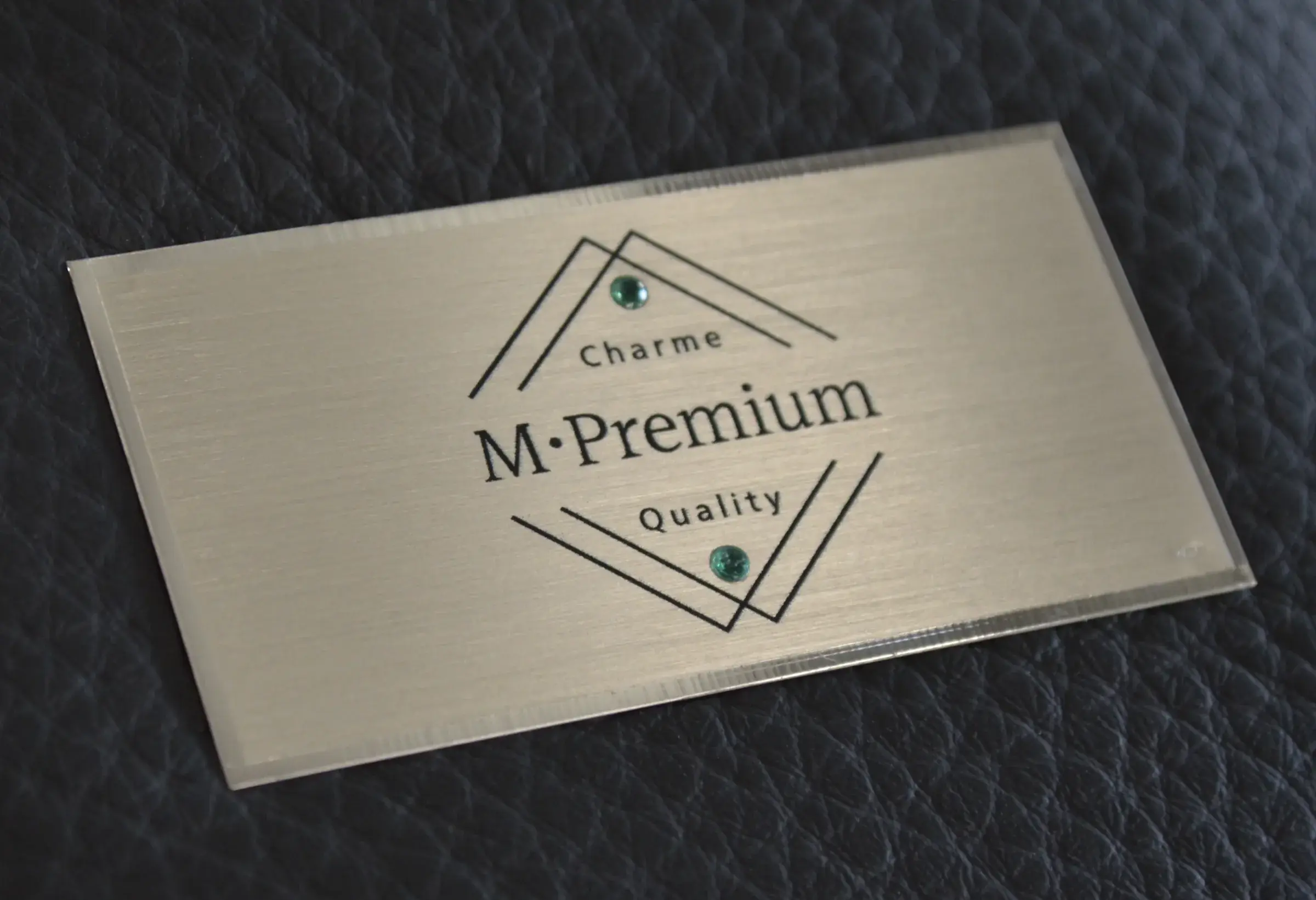 Placca M•Premium su pelle nera, con le pietre verdi incastonate