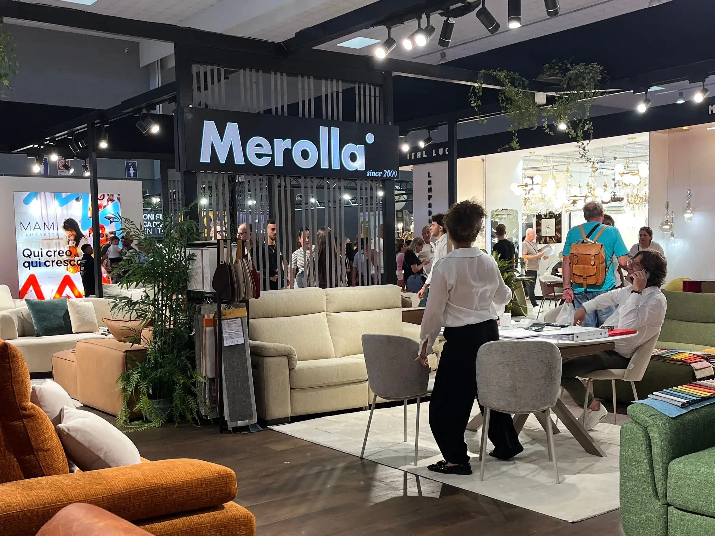 Lo stand Merolla alla Fiera del Levante 2026, con l’insegna luminosa, i divani esposti e il tavolo dei campioni di tessuto