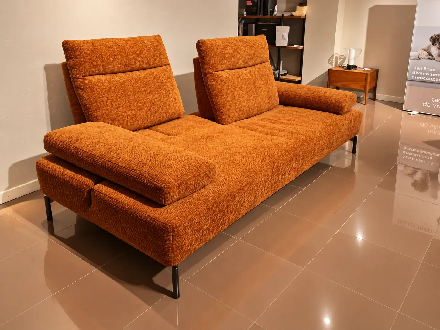 Divano arancione con poggiatesta regolabili e piedini in metallo nello showroom
