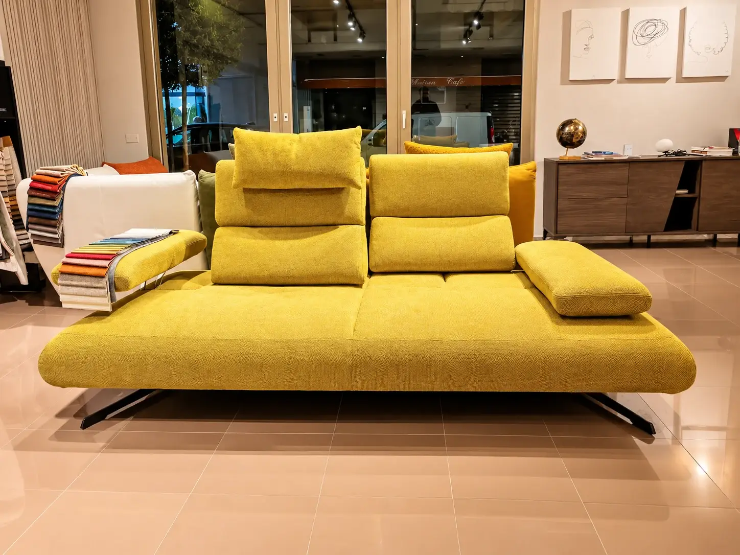 Divano giallo senape con braccioli traslanti nello showroom illuminato